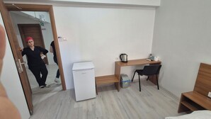 Habitación de hotel pequeña con escritorio de madera, refrigerador compacto, una silla, cama y un cubo de basura.