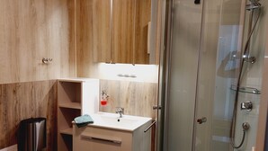 A modern bathroom with a glass shower enclosure, a white sink, and wooden cabinetry. - Apartmenthaus Am Kornfeld  (Lünen)