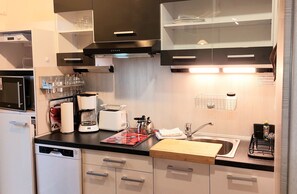 A modern kitchen with a dishwasher, coffee maker, toaster, and a cutting board.