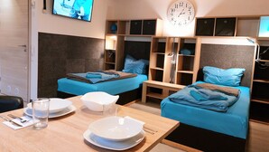 A hotel room with two beds, a dining table with plates and cutlery, a clock, and a television. - Apartmenthaus Am Kornfeld  (Lünen)