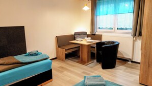 A small, cozy room with a bed, a table, a chair, and a window with curtains. - Apartmenthaus Am Kornfeld  (Lünen)