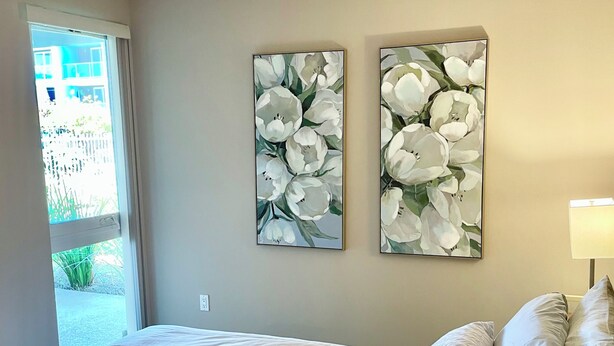 Une chambre à coucher avec un lit, des oreillers et deux tableaux représentant des motifs floraux, accrochés au mur.