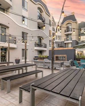 An outdoor patio area with benches, string lights, and a building with balconies.