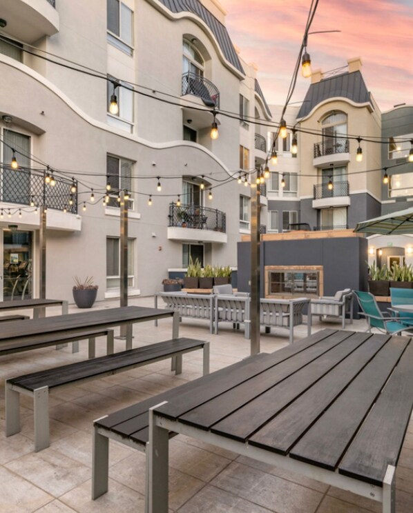 An outdoor patio area with benches, string lights, and a building with balconies.