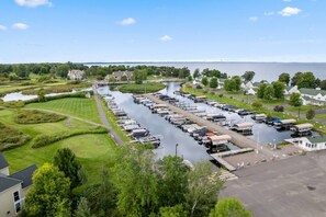 Una marina con barcos amarrados, un río y casas al fondo.