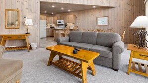 A cozy living room with a sofa, a wooden coffee table, and a kitchen in the background. - The Villages @Izatys Cabin Week 45 (Onamia)
