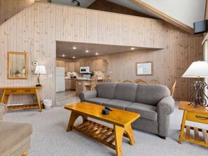 Ein gemütliches Wohnzimmer mit einer Couch, einem Holztisch und einer Küche im Hintergrund.