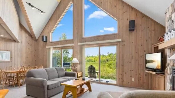 A spacious living room with a high ceiling, large windows, a fireplace, and a television. - The Villages @Izatys Cabin Week 45 (Onamia)