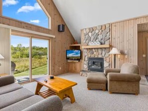 Un salón moderno con chimenea de piedra, televisor y una ventana grande con vistas a un paisaje natural.