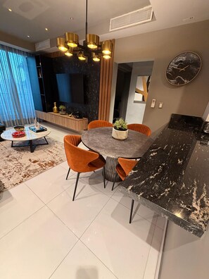 A modern kitchen with a black marble countertop, a round dining table with orange chairs, and a pendant light fixture.