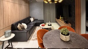 Een moderne woonkamer met een hoekbank, een ronde eettafel met stoelen, een klein bijzettafeltje en een hanglamp.