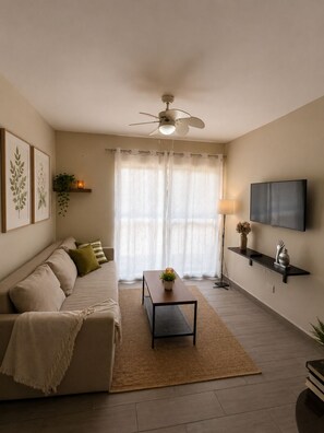 A living room with a sofa, a coffee table, a TV, and a ceiling fan. - Warm and Cozy Apartment in Punta Cana (Punta Cana)