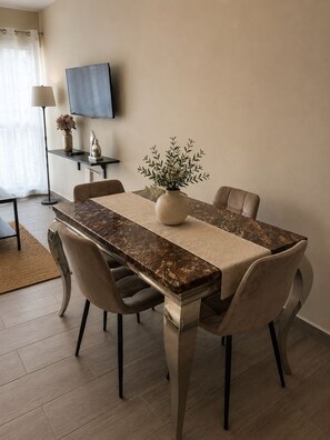 A dining area with a marble table, cushioned chairs, a vase with greenery, a lamp, and a TV on the wall. - Warm and Cozy Apartment in Punta Cana (Punta Cana)