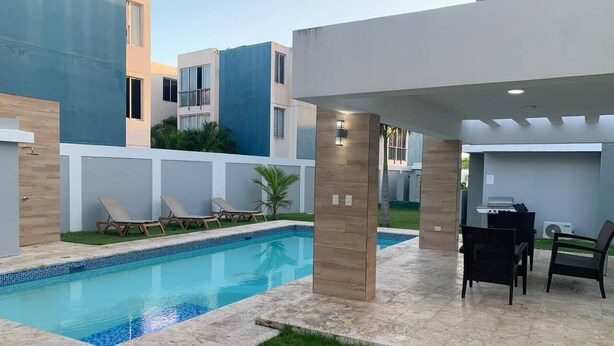 Uma área de piscina moderna ao ar livre, com espreguiçadeiras, um espaço de estar coberto e um gramado bem cuidado.