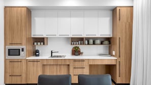 A modern kitchen with wooden cabinets, a built-in microwave, a sink, and a small dining area with two chairs.