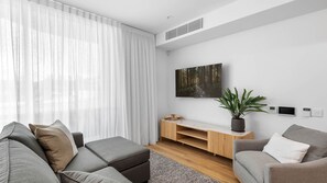 Ein modernes Wohnzimmer mit einer Couch, einem Couchtisch, einem Fernseher, einer Pflanze und einem Kamin.