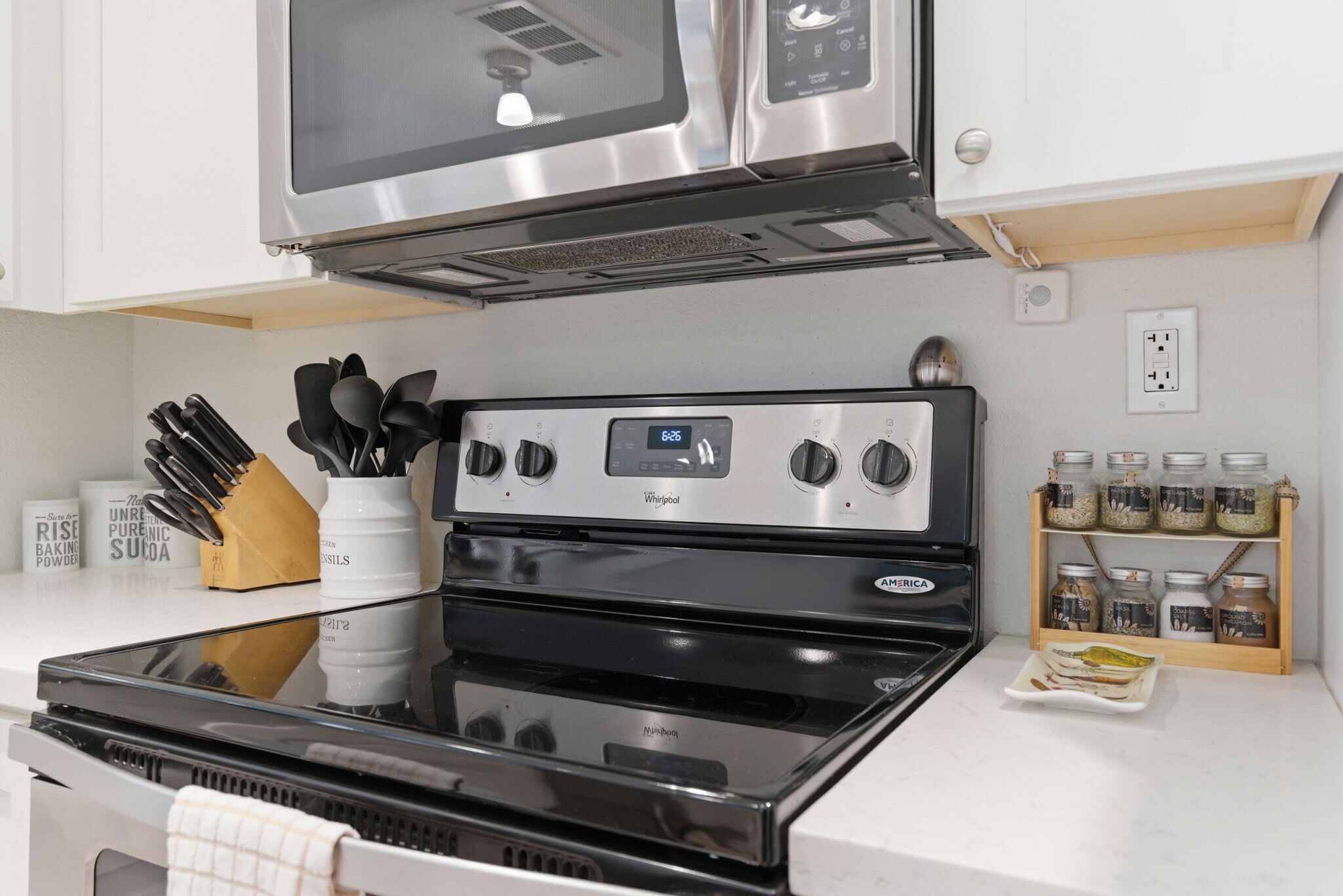 A kitchen with a black stove, a microwave above it, and a wooden spice rack with jars.