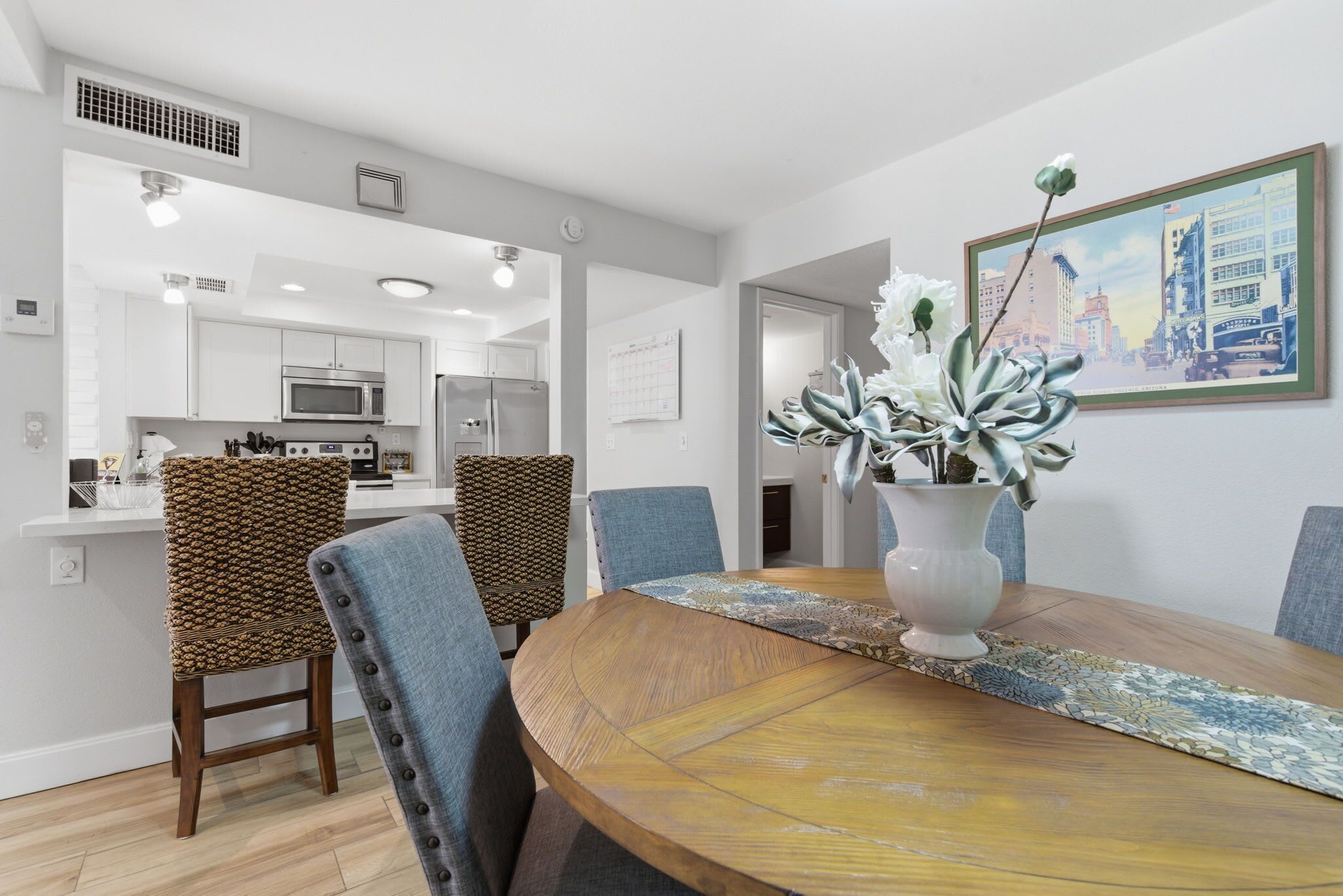 A dining area with a wooden table, chairs, a vase with flowers, and a cityscape painting on the wall.