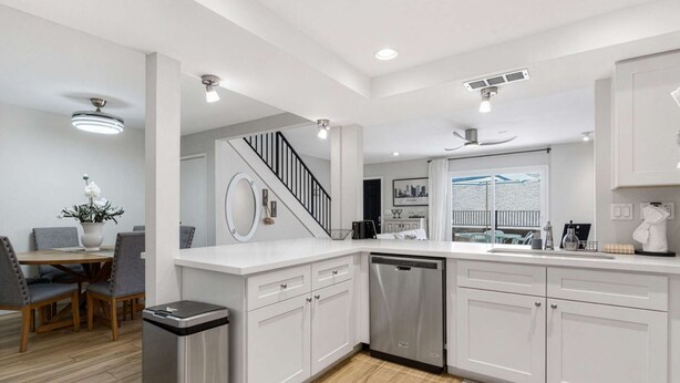 A modern kitchen with white cabinetry, a stainless steel dishwasher, and a dining area with a table and chairs. - Terra - Pool - Walk to Entertainment District (Scottsdale)