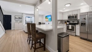A modern kitchen with stainless steel appliances, a white countertop, and a seating area with wicker chairs. - Terra - Pool - Walk to Entertainment District (Scottsdale)