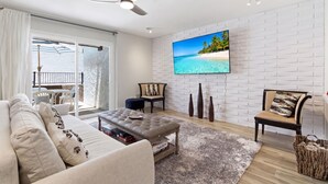 A living room with a white brick wall, a flat-screen TV, a ceiling fan, a sofa, a coffee table, and a view of a balcony. - Terra - Pool - Walk to Entertainment District (Scottsdale)