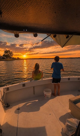 A boat with two people on deck, a bucket, and a sunset view.. Sleep on the water! Cozy Yacht Experience 5 mins from the beach.