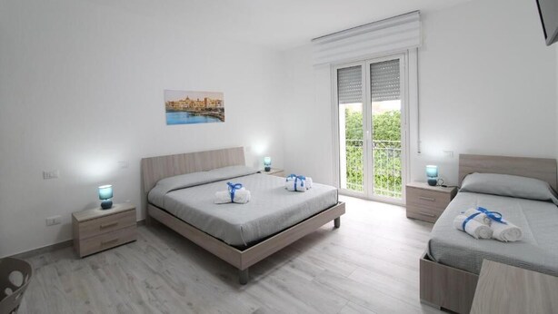 A modern bedroom with a large bed, bedside tables, a window with a view, and a painting on the wall.