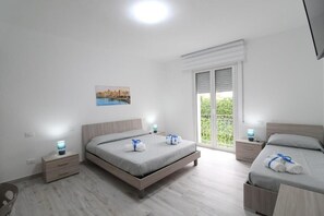 A modern bedroom with a large bed, bedside tables, a window with a view, and a painting on the wall.