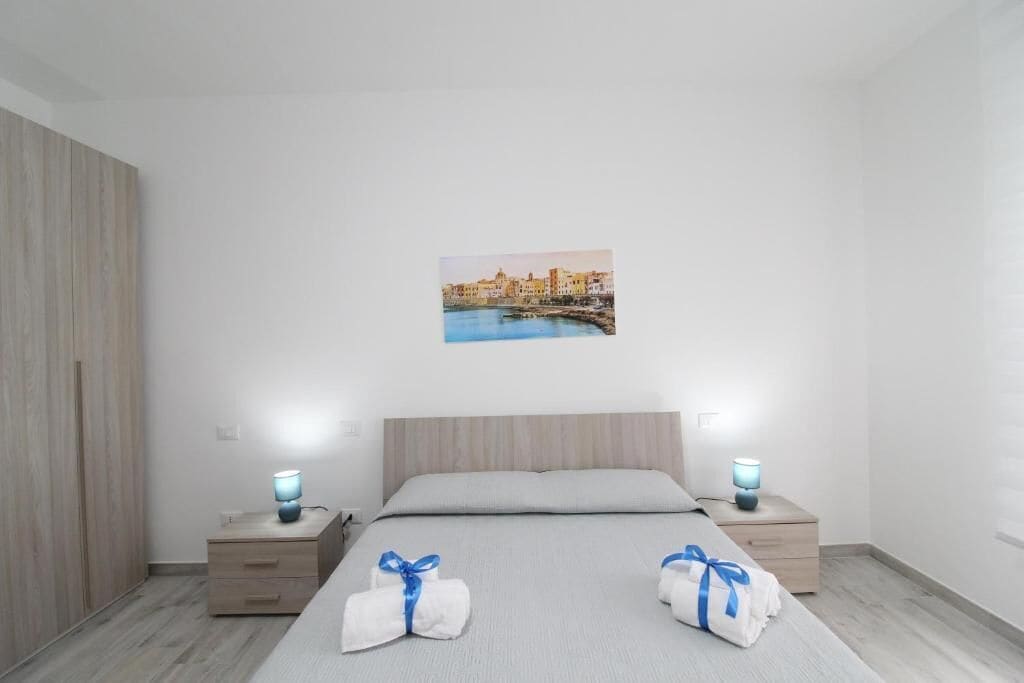 Habitación de hotel con cama, dos mesitas de noche, un armario de madera y un cuadro colgado en la pared.
