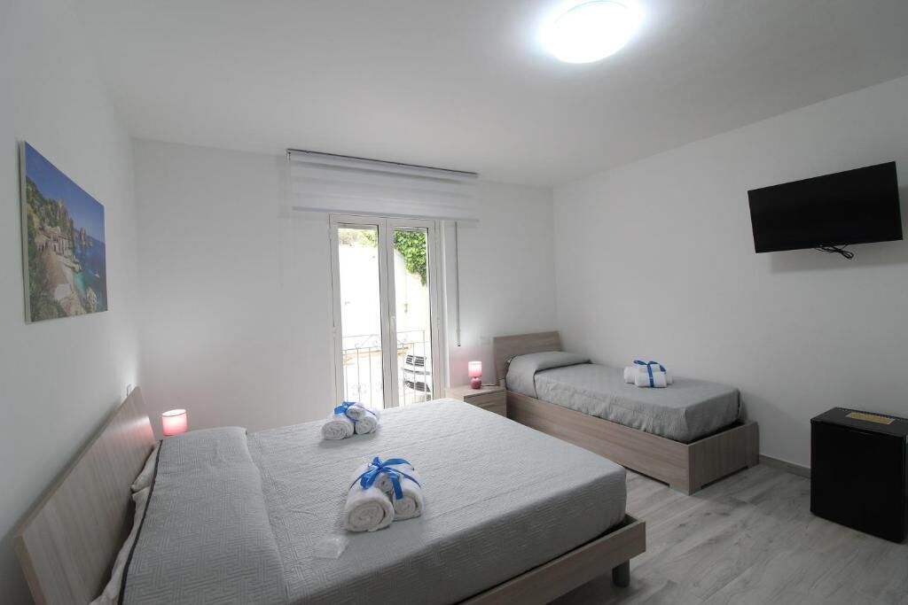 Habitación de hotel con dos camas, un televisor, una ventana con persianas y un cuadro en la pared.