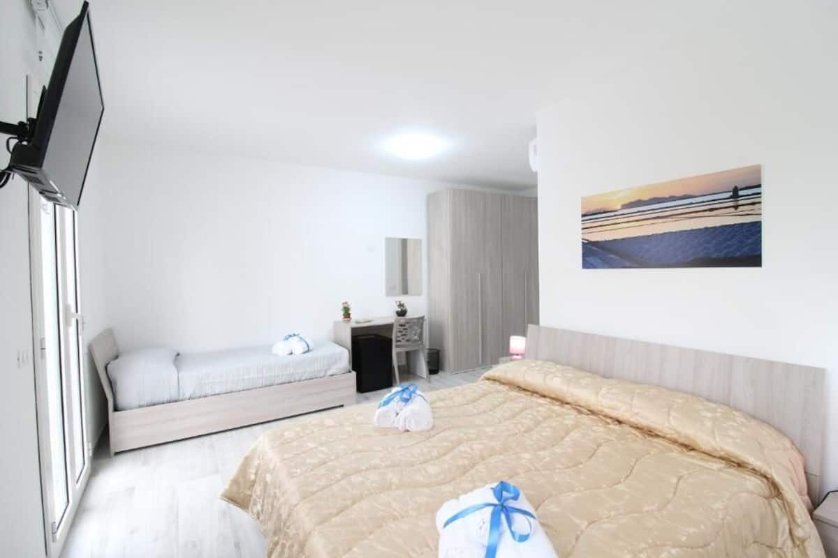 Habitación de hotel con cama, escritorio, silla, televisor y un cuadro en la pared.