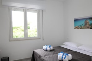 Een hotelkamer met een bed, een raam met uitzicht op groen en een schilderij aan de muur.