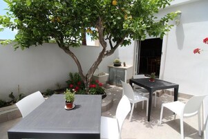 Un patio con una mesa y sillas, un árbol con flores rojas y una pequeña planta en maceta sobre la mesa.