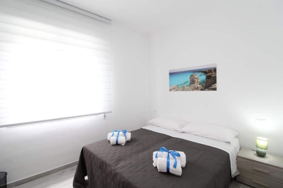 Una habitación de hotel con cama, mesita de noche, lámpara y ventana con persianas.