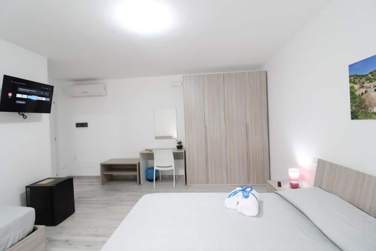 Una habitación de hotel con cama, escritorio, silla, televisor y armario.