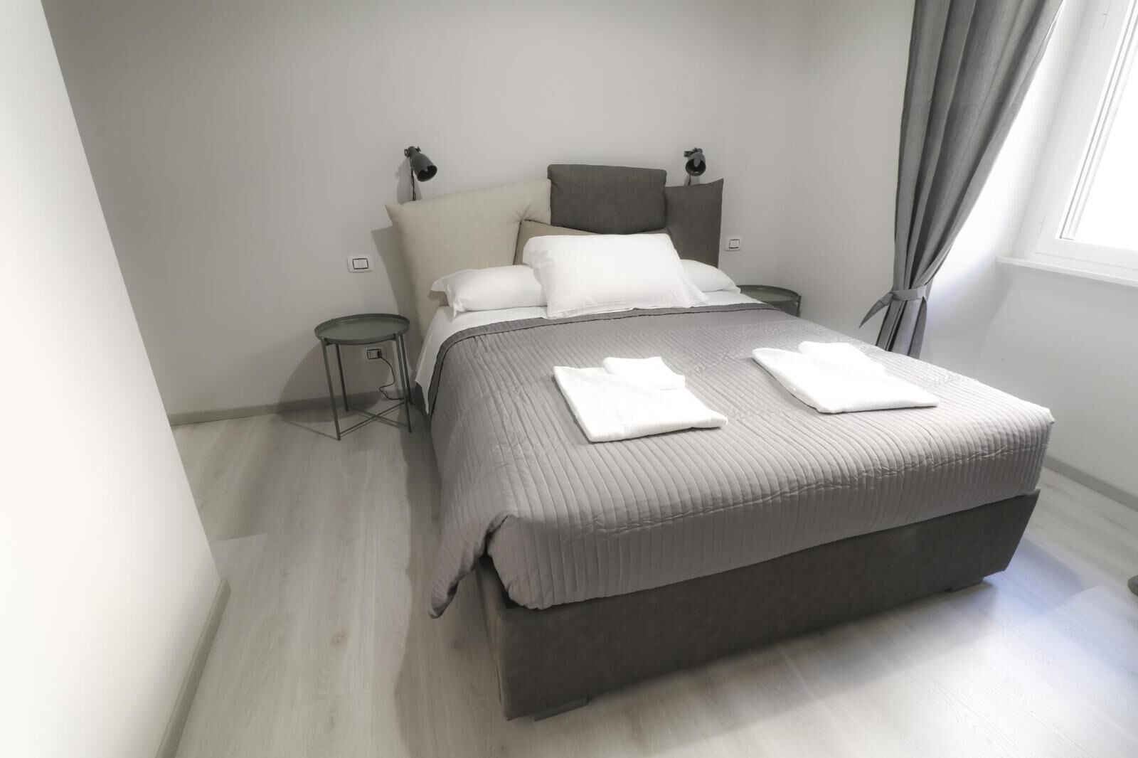 A modern bedroom with a large bed, bedside tables, a lamp, and a window with curtains.