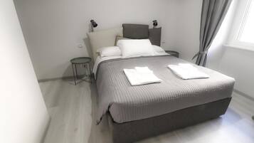 A modern bedroom with a large bed, bedside tables, a lamp, and a window with curtains.