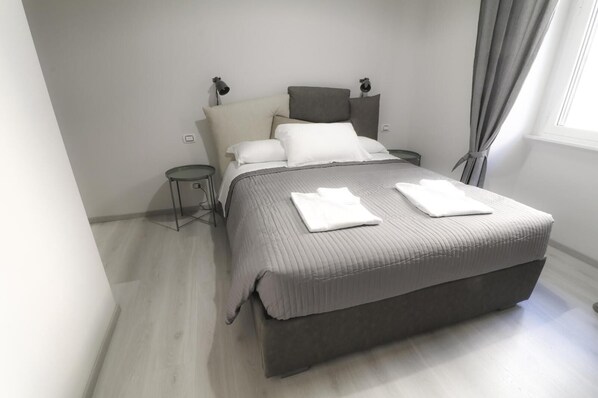 A modern bedroom with a large bed, bedside tables, a lamp, and a window with curtains. - Charming Double room Standard (Roma)