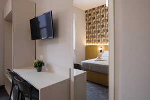 Una habitación de hotel con escritorio, televisor, cama con cabecera y una pared con diseño decorativo.