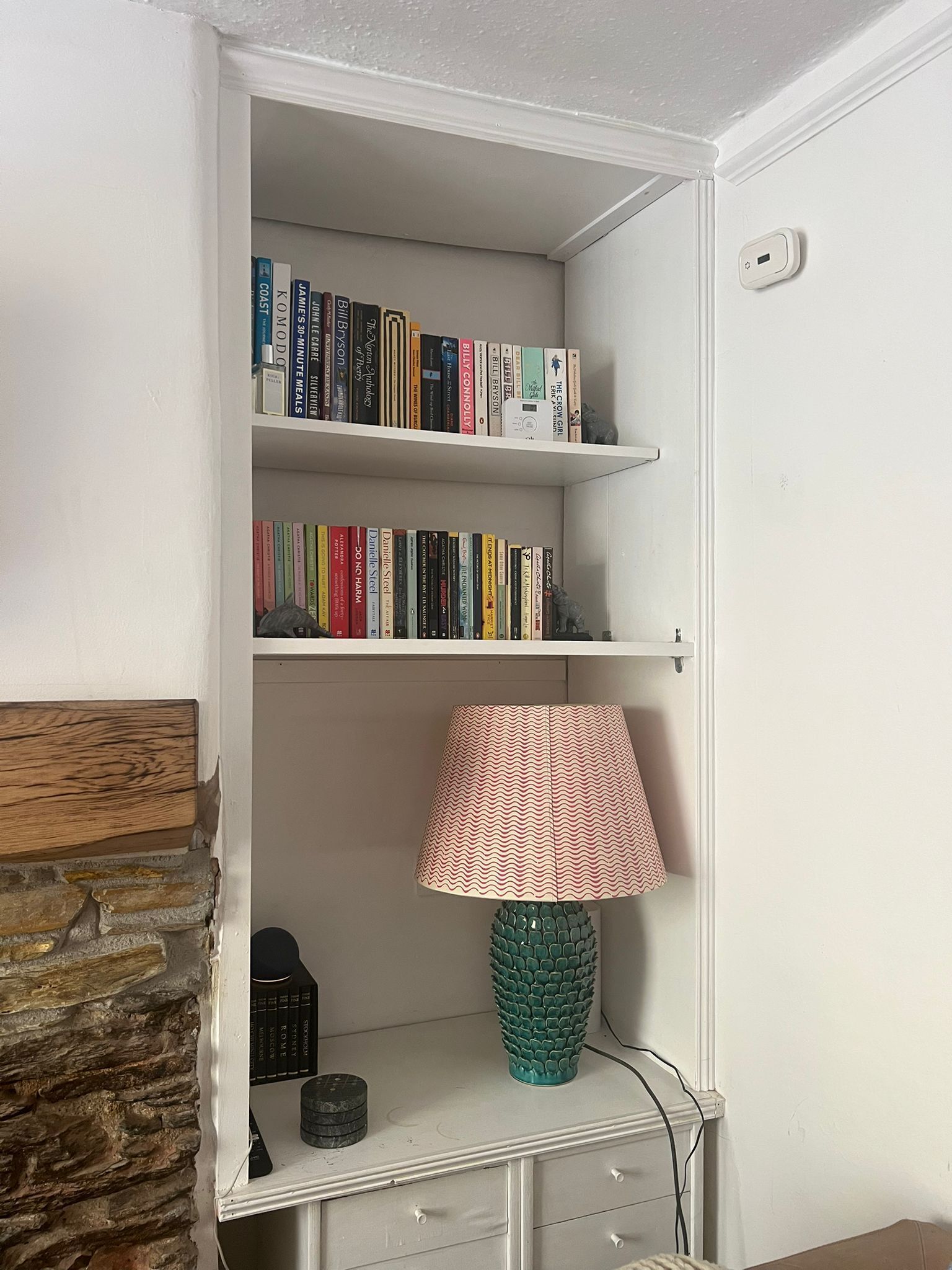 Een boekenplank met boeken, een lamp en een klein decoratief object op een wit schap.