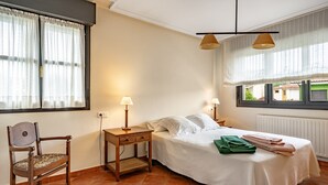 Une chambre à coucher avec un lit, deux lampes de chevet, une chaise, une table de chevet et une fenêtre avec des rideaux.