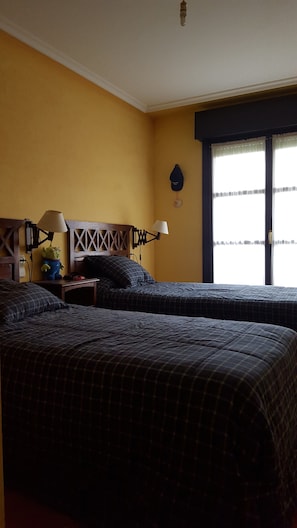A hotel room with two beds, a nightstand with a lamp, a wall clock, and a window with curtains.