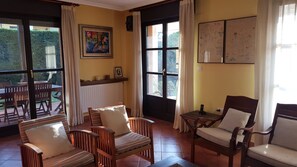 Habitació amb zona de menjador, sofà, cadira, taula i finestra amb cortines.