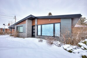 A modern house with a stone facade, large windows, and a snow-covered landscape.