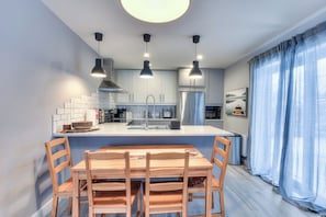 A modern kitchen with a central island, pendant lighting, and a dining area with wooden chairs.