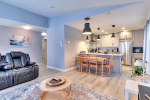 A modern living room with a sofa, dining table, and kitchen in the background.