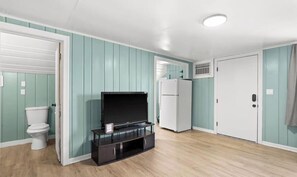 A room with teal walls, a wooden floor, a television on a black stand, a white door, and a white refrigerator.