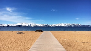 A beach with a wooden walkway leading to a bench, overlooking a body of water and snow-capped mountains. - Mountain & Lake Vacation with Spacious 2BR at South Shore (Zephyr Cove)