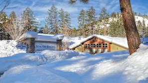 A lodge with a stone entrance, a wooden building, and snow-covered surroundings.