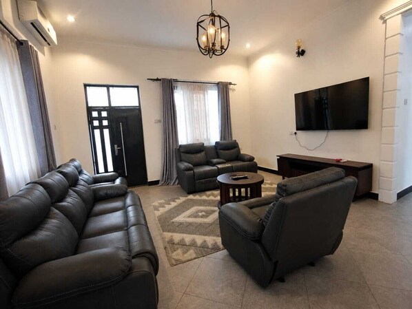 A living room with a sectional sofa, a recliner, a coffee table, a flat-screen TV, and a large window with curtains.